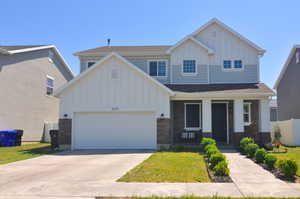 Craftsman-style home with board and batten siding, covered porch, concrete driveway, an attached garage, and a front lawn