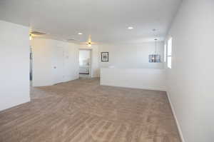 Spare room featuring light colored carpet, a chandelier, baseboards, and recessed lighting