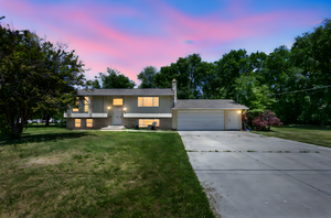 Bi-level home featuring concrete driveway, a garage, brick siding, and a front yard
