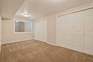 Unfurnished bedroom with carpet floors, two closets, and baseboards