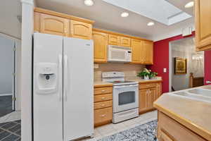 Kitchen with white appliances, a skylight, light tile patterned flooring, light countertops, and recessed lighting