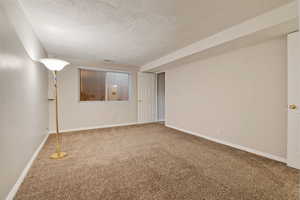 Carpeted empty room with a textured ceiling and baseboards