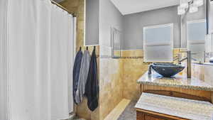 Full bath featuring curtained shower, vanity, tile walls, and wainscoting