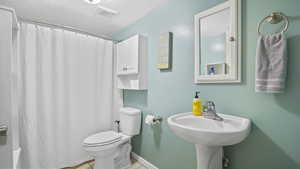 Full bath featuring toilet, a shower with curtain, tile patterned floors, baseboards, and a textured ceiling