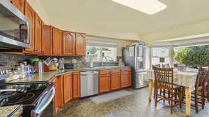 Kitchen featuring appliances with stainless steel finishes, a sink, backsplash, and brown cabinetry