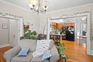 Living area featuring a chandelier, crown molding, light wood-type flooring, and baseboards