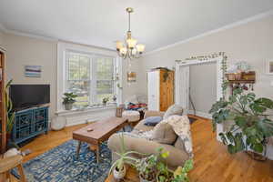 Living area with a chandelier, wood finished floors, ornamental molding, and baseboards