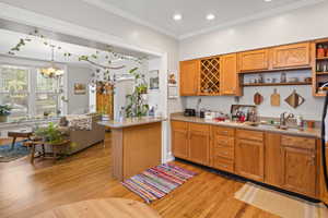 Kitchen featuring open shelves, a sink, light wood-style flooring, brown cabinets, and crown molding