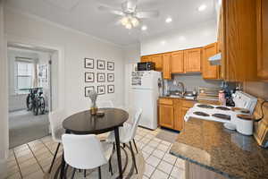 Kitchen featuring white appliances, a sink, under cabinet range hood, a ceiling fan, and light tile patterned floors