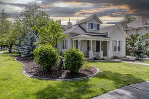 View of front facade featuring a porch, a chimney, a front yard, a shingled roof, and stucco siding