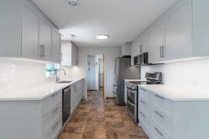 Kitchen with stainless steel appliances, a sink, stone finish floors, backsplash, and light countertops