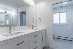 Bathroom featuring baseboard heating, double vanity, and tile patterned floors