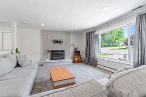 Carpeted living area featuring a baseboard radiator, a brick fireplace, and recessed lighting
