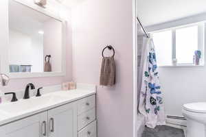 Full bathroom featuring baseboard heating, vanity, toilet, a shower with curtain, and tile patterned flooring