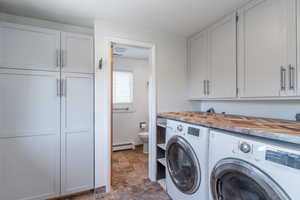 Washroom with washer and clothes dryer, a baseboard heating unit, cabinet space, and stone finish floors