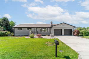Ranch-style home featuring an attached garage, a front yard, driveway, and a chimney
