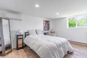 Bedroom with an AC wall unit, a baseboard radiator, wood finished floors, and recessed lighting