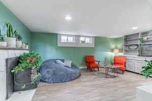 Living area with light wood-type flooring, a baseboard radiator, a fireplace, and recessed lighting