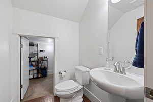 Bathroom featuring lofted ceiling, a sink, toilet, and wood finished floors