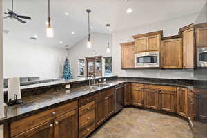 Kitchen featuring stainless steel appliances, a sink, ceiling fan, decorative light fixtures, and high vaulted ceiling
