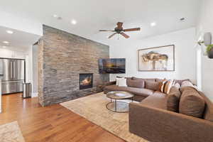 Living room with a ceiling fan, light wood-style floors, a stone fireplace, and recessed lighting
