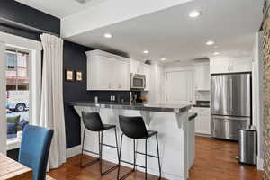 Kitchen featuring appliances with stainless steel finishes, a peninsula, white cabinetry, a kitchen breakfast bar, and recessed lighting