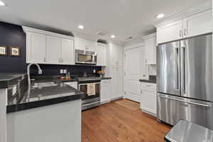 Kitchen featuring appliances with stainless steel finishes, a sink, recessed lighting, white cabinets, and dark countertops