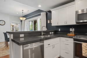 Kitchen featuring stainless steel appliances, a sink, a peninsula, white cabinets, and wood finished floors