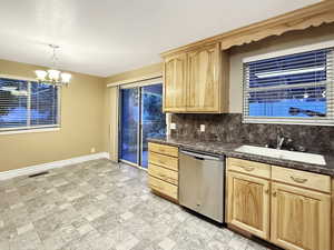 Kitchen with stainless steel dishwasher, light brown cabinets, baseboards, a sink, and a chandelier