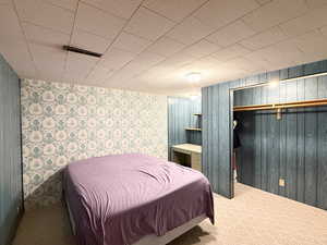 Carpeted bedroom with wallpapered walls, wood walls, and a closet