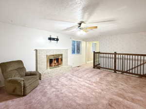 Unfurnished room with a ceiling fan, a textured ceiling, carpet, a brick fireplace, and wallpapered walls