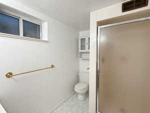 Bathroom with toilet, a stall shower, baseboards, a textured ceiling, and tile patterned floors