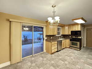 Kitchen with appliances with stainless steel finishes, a chandelier, light brown cabinets, tasteful backsplash, and stone finish floors