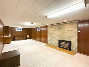 Finished basement featuring wooden walls, carpet, and a brick fireplace