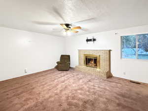 Unfurnished living room featuring ceiling fan, a brick fireplace, a textured ceiling, and carpet