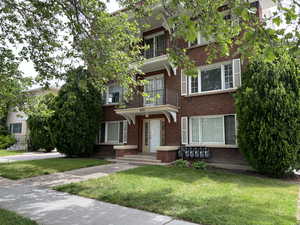 View of front facade with brick siding, a front lawn, and a balcony