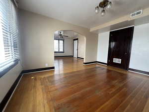 Spare room featuring arched walkways, wood-type flooring, a ceiling fan, and baseboards