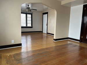 Unfurnished room with arched walkways, ceiling fan, hardwood / wood-style flooring, and baseboards