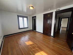 Unfurnished bedroom with wood-type flooring, two closets, and baseboards