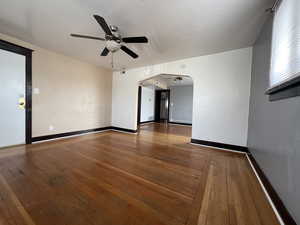 Spare room with arched walkways, a ceiling fan, wood-type flooring, and baseboards