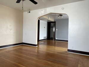 Empty room featuring arched walkways, ceiling fan, wood-type flooring, baseboards, and a smoke detector