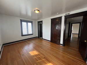 Unfurnished bedroom featuring hardwood / wood-style floors, multiple closets, and baseboards
