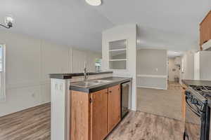 Kitchen featuring stainless steel dishwasher, a sink, dark countertops, lofted ceiling, and black gas range