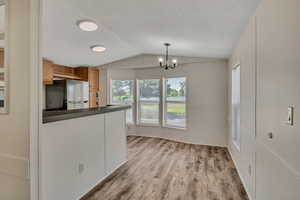 Kitchen featuring freestanding refrigerator, dark countertops, vaulted ceiling, brown cabinetry, and light wood-type flooring
