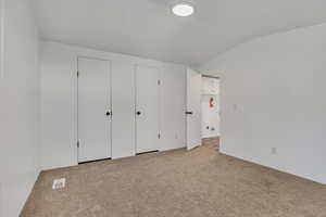 Unfurnished bedroom with light carpet, vaulted ceiling, and multiple closets