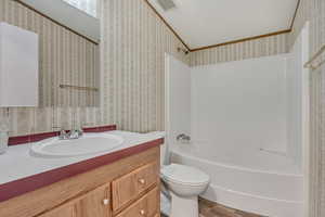 Bathroom with wood finished floors, toilet, vanity, shower / bathtub combination, and wallpapered walls