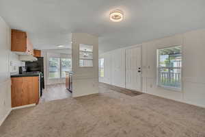 Kitchen with light colored carpet, vaulted ceiling, open floor plan, brown cabinets, and gas range