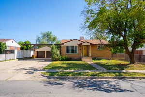 View of front of property featuring brick siding, driveway, a chimney, and a carport