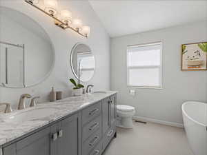 Bathroom with double vanity, a freestanding tub, toilet, lofted ceiling, and tile patterned flooring