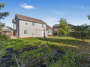Rear view of house featuring a vegetable garden, stucco siding, roof with shingles, and a patio